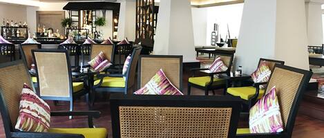 A lobby with wicker chairs and yellow cushions, a bar area with bottles, and a decorative wall.