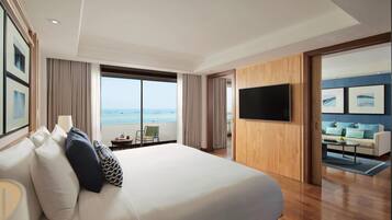A hotel room with a large bed, a television, a view of the sea, and a balcony with a chair.