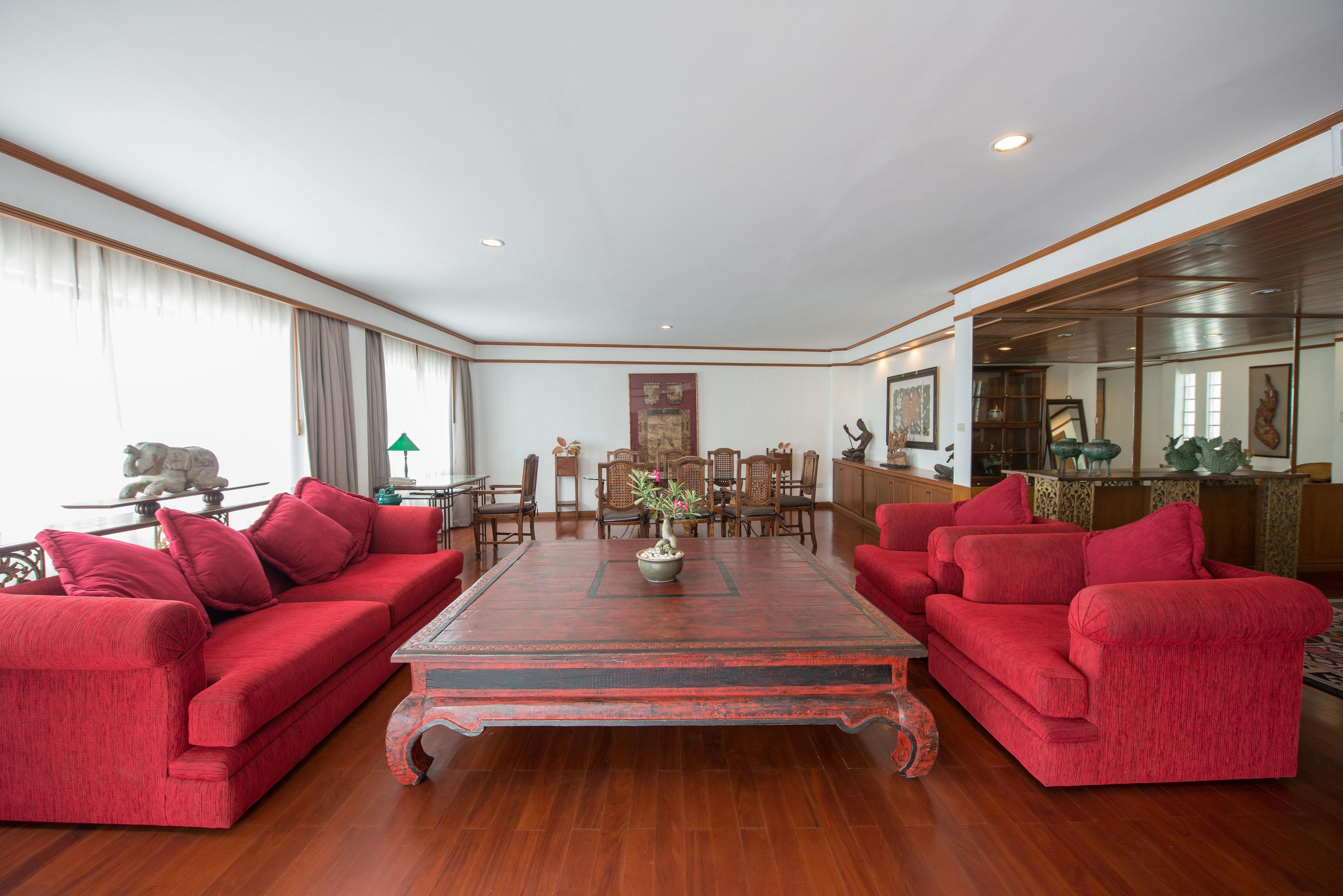 A spacious room with a large wooden coffee table, red sofas, and a dining area with wooden chairs and a table.
