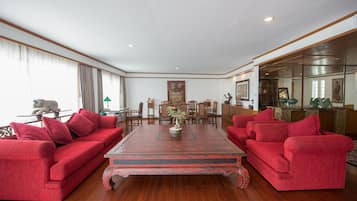 A spacious room with a large wooden coffee table, red sofas, and a dining area with wooden chairs and a table.