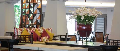 A lobby with a sofa set, a large potted plant, and a patterned rug.
