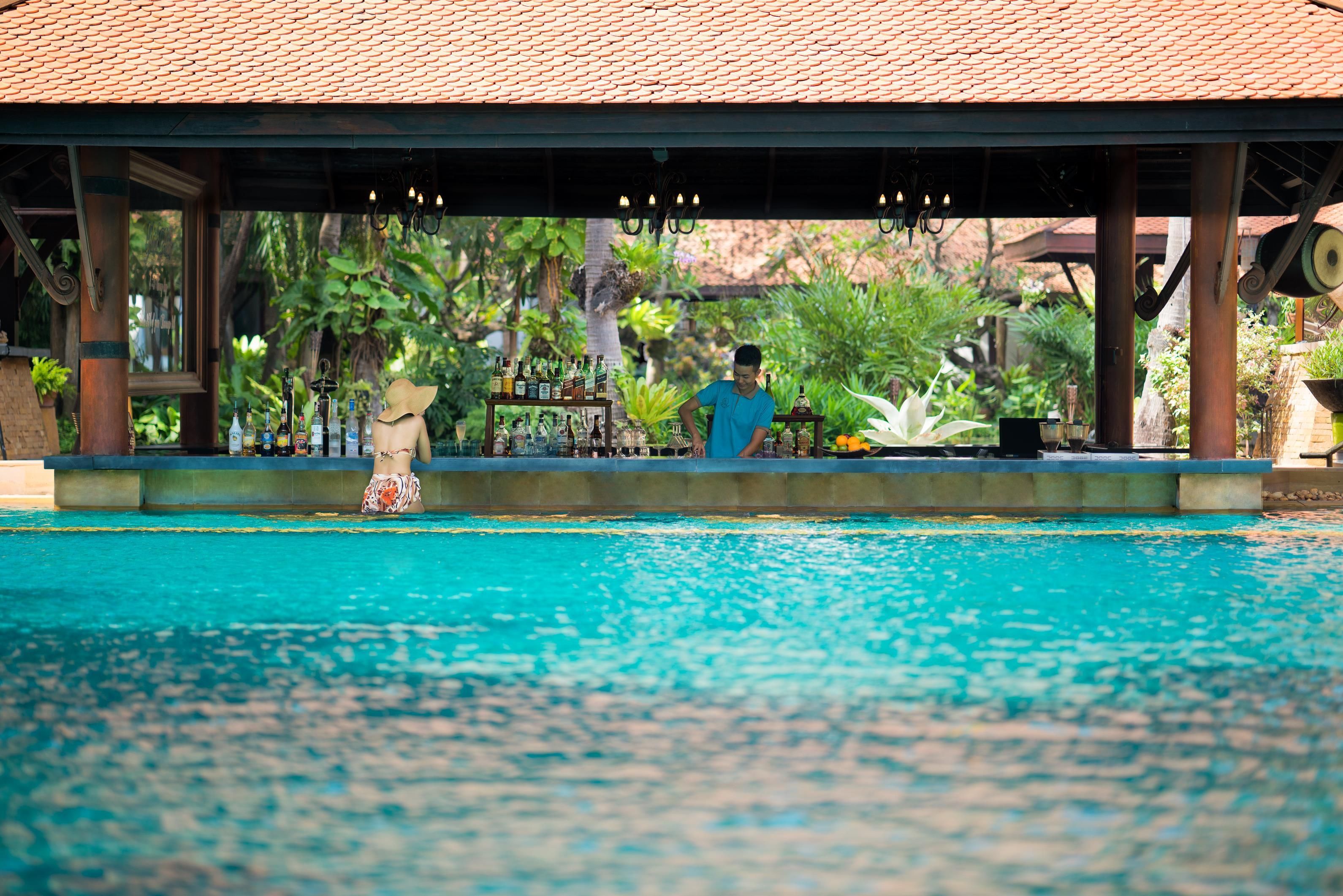 Un área de piscina con zona de estar cubierta y bar.
