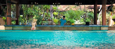 Un área de piscina con zona de estar cubierta y bar.