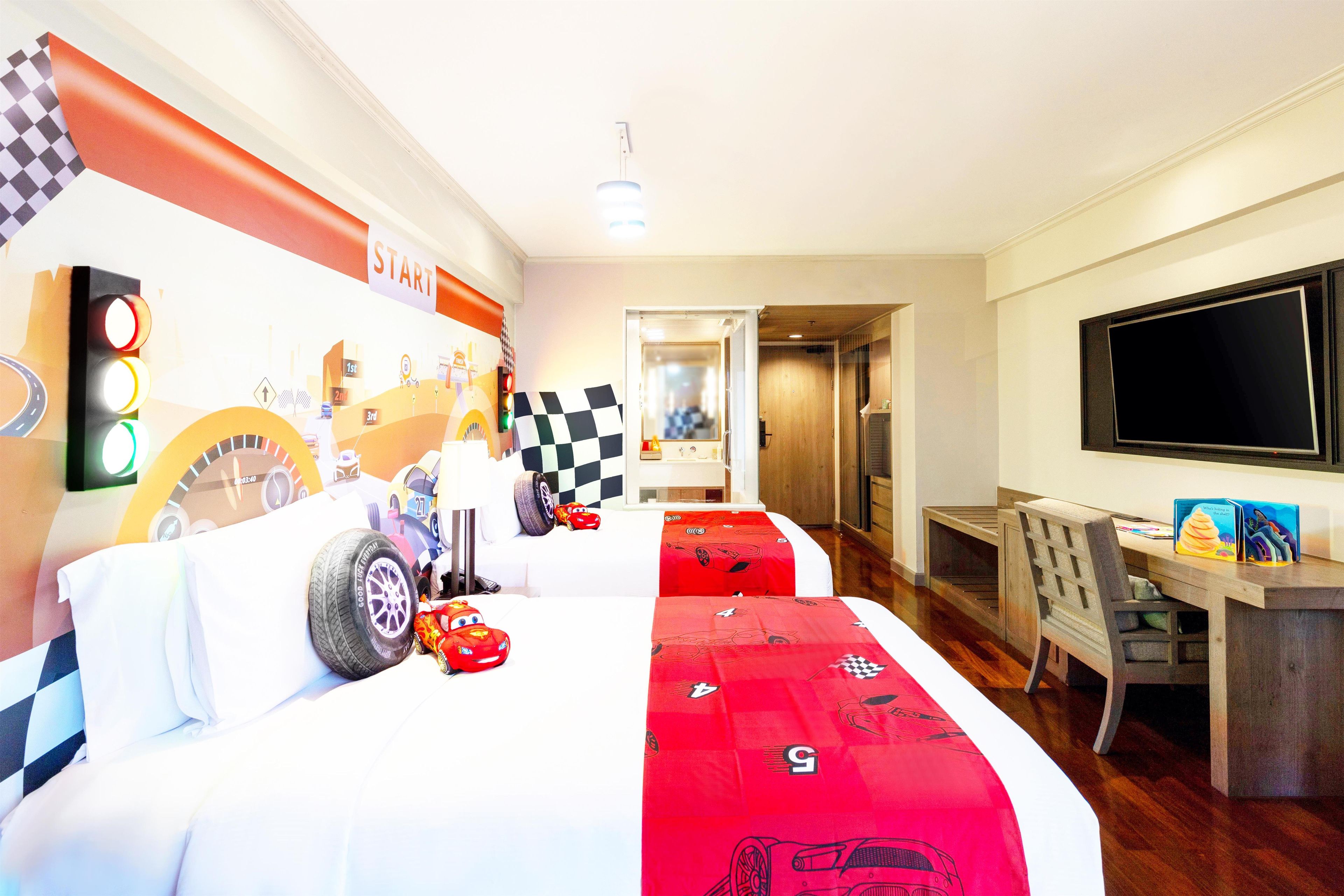 Habitación de hotel con temática de circuito de carreras, que incluye una cama con ropa de cama a cuadros, un coche de carreras sobre la cama y una decoración de circuito en la pared.