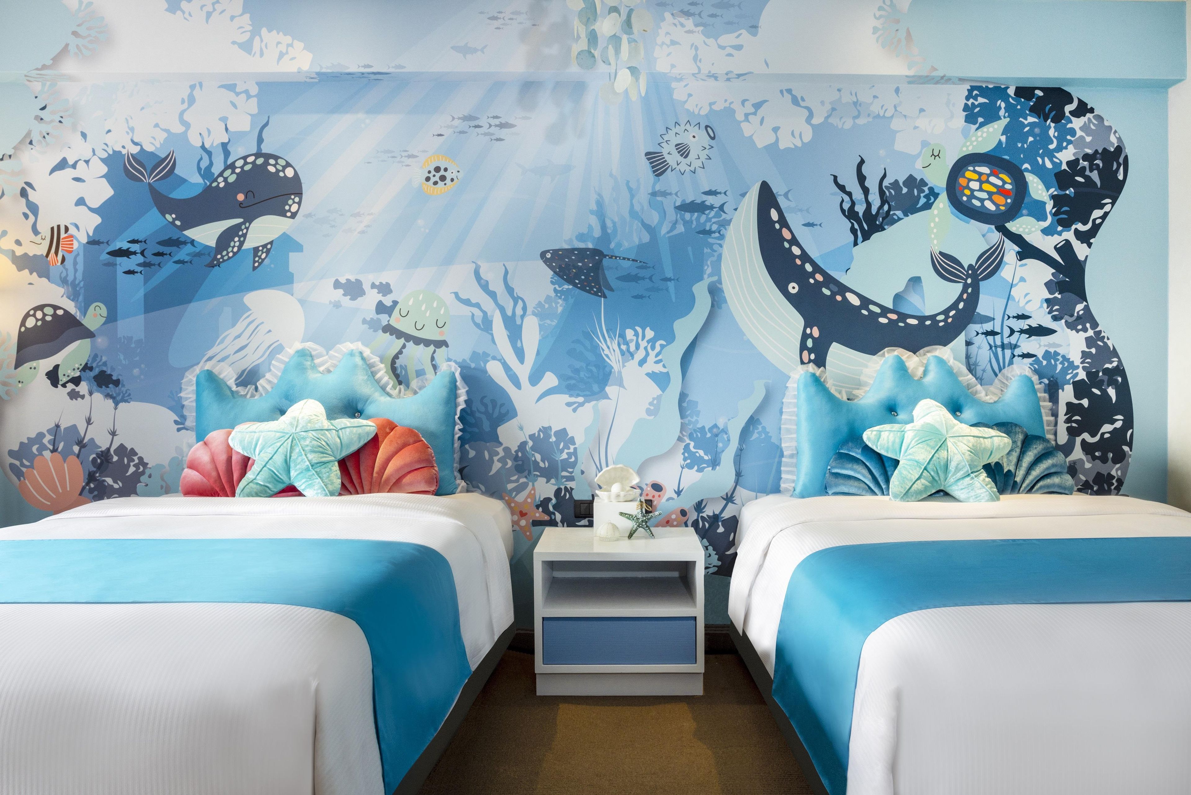 A bedroom with two beds, a nightstand, and a mural of an underwater scene.
