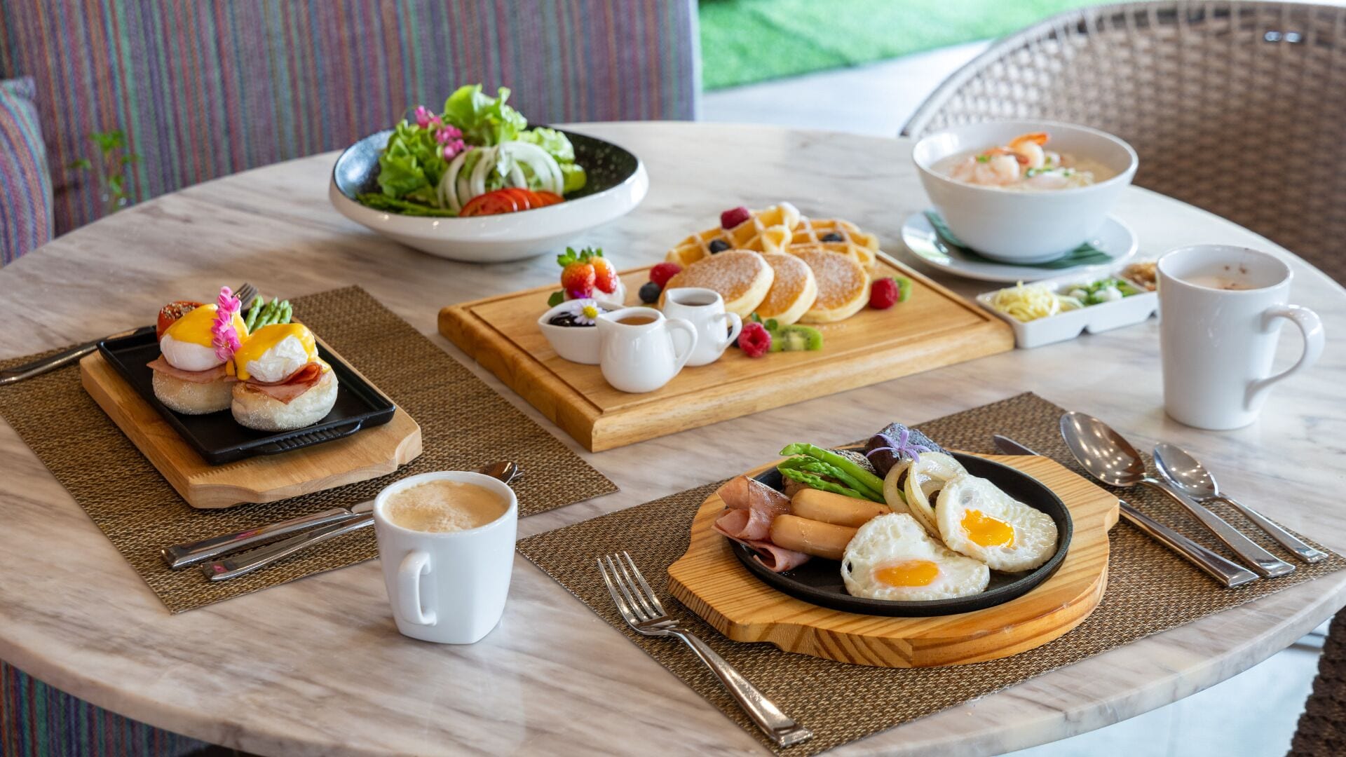 A round dining table with breakfast items including pancakes, eggs, and a salad.