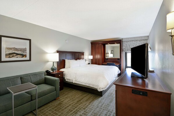 A hotel room with a bed, a desk, a chair, a small table, a lamp, a TV, and a framed picture on the wall. - Hampton Inn Detroit/Madison Heights/South Troy (Madison Heights)