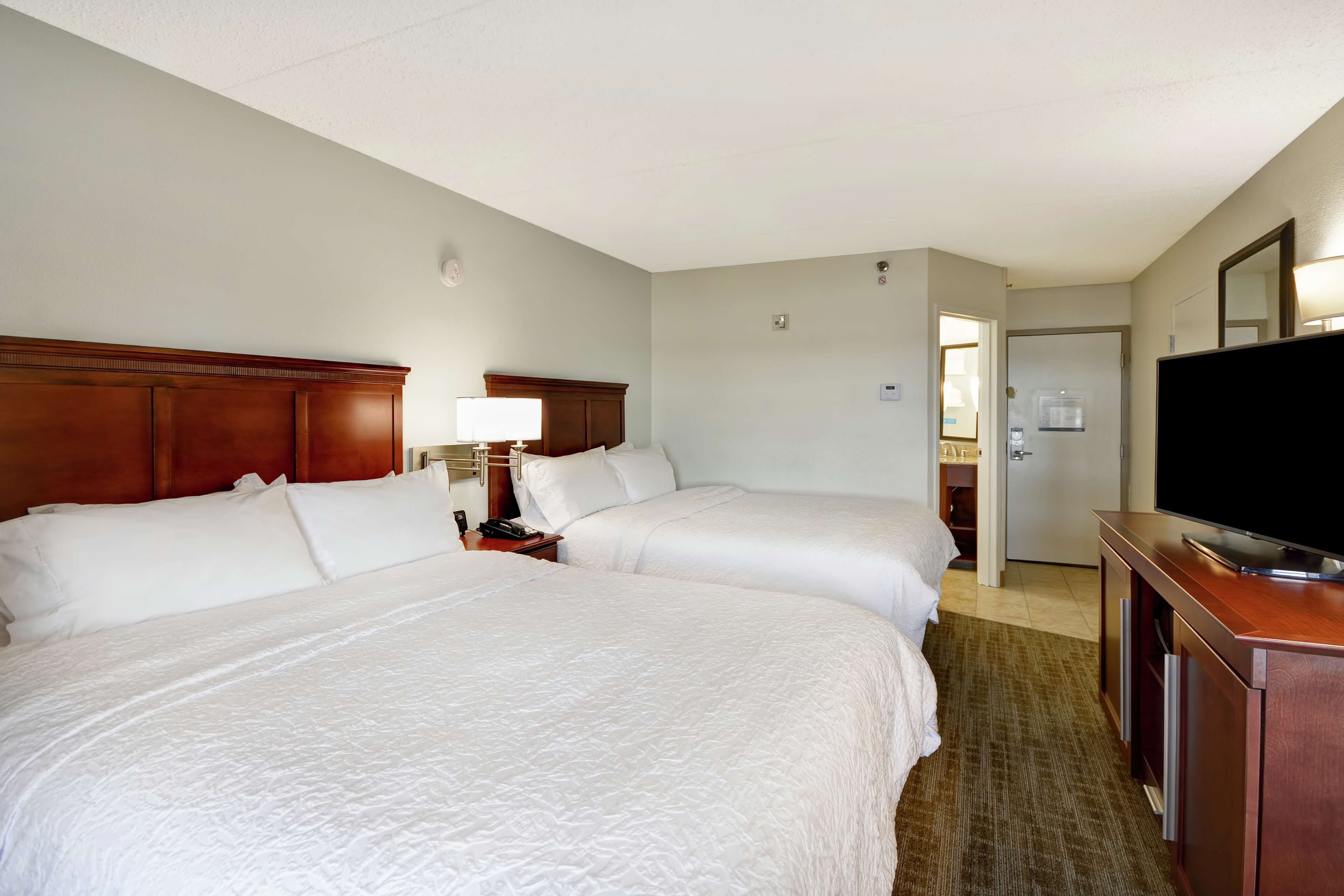 A hotel room with two beds, a TV, a desk, and a bathroom visible through an open door.