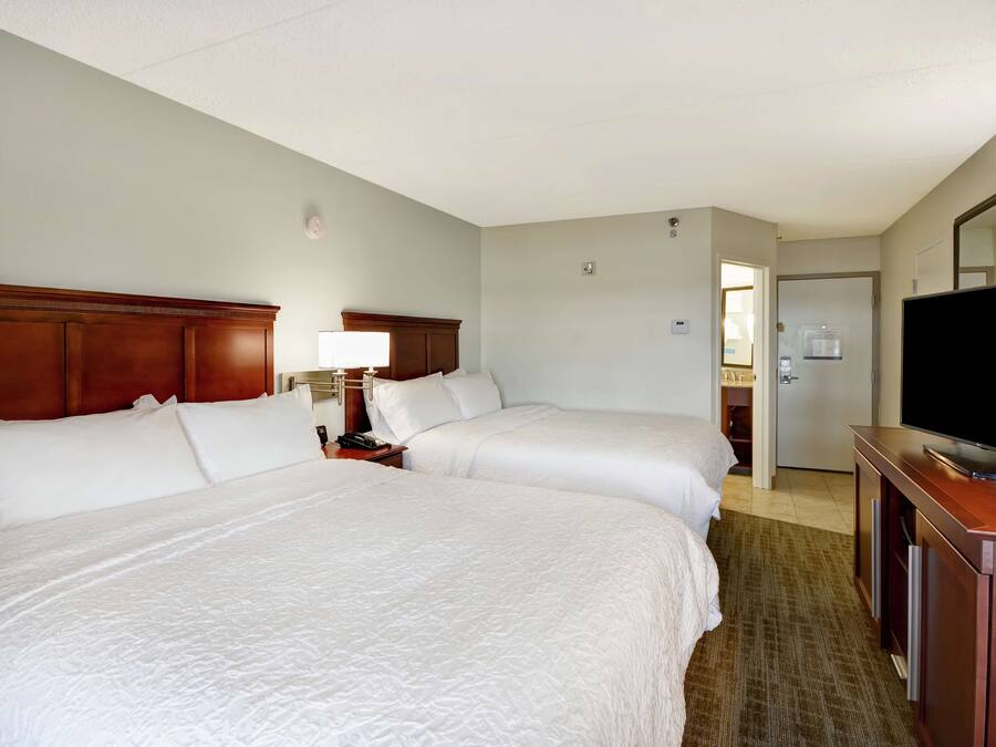 A hotel room with two beds, a TV, a desk, and a bathroom visible through an open door.