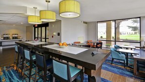 A modern hotel lobby with a central bar area, seating, and large windows offering a view of the outdoors. - Hampton Inn Detroit/Madison Heights/South Troy (Madison Heights)