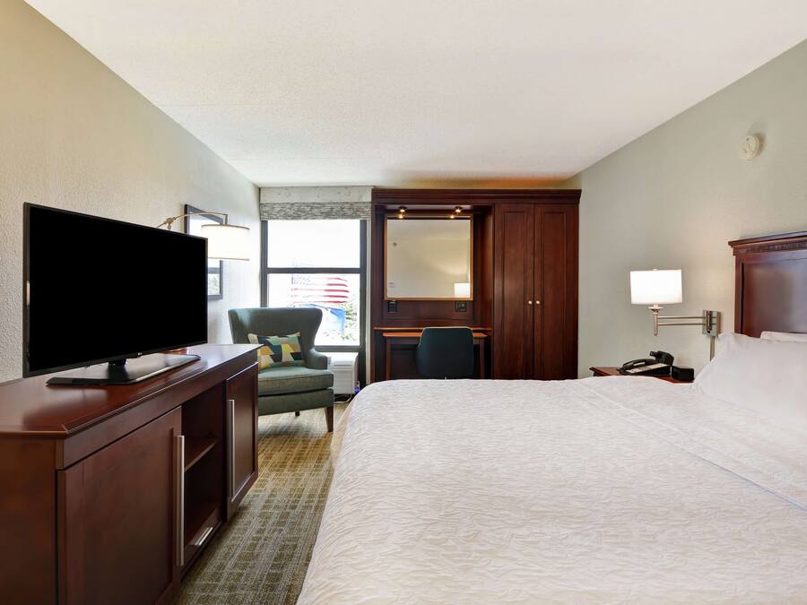 Ein Hotelzimmer mit einem großen Bett, einem Flachbildfernseher auf einer Holzkommode, einem Schreibtisch mit Stuhl und einem großen Spiegel.