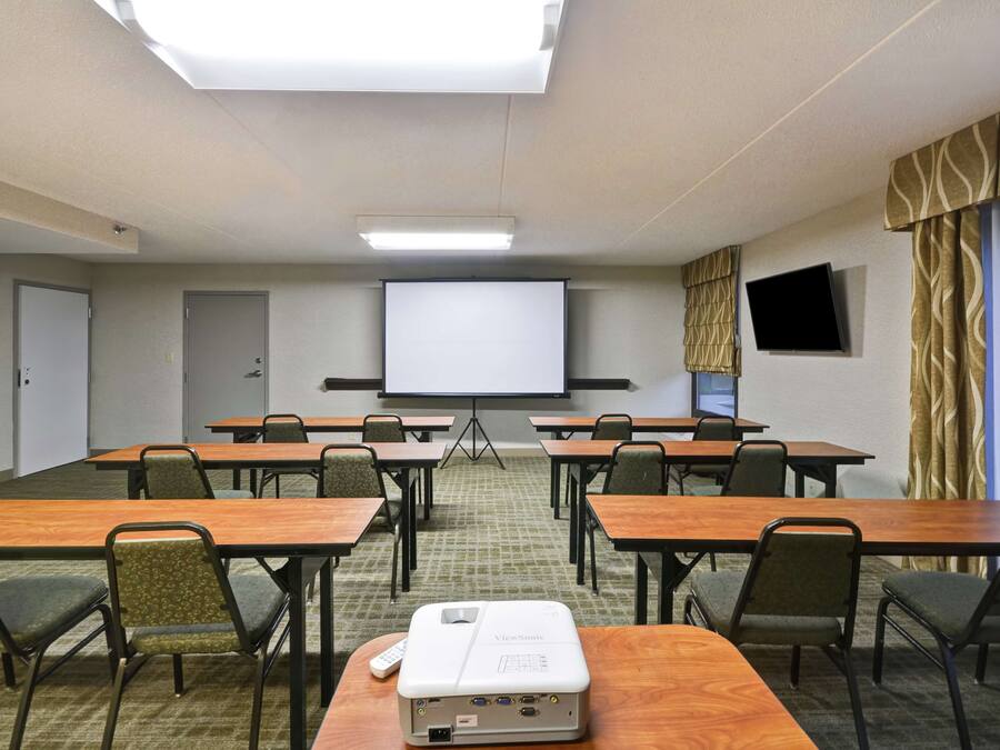 A conference room with a large screen, multiple tables, and chairs.