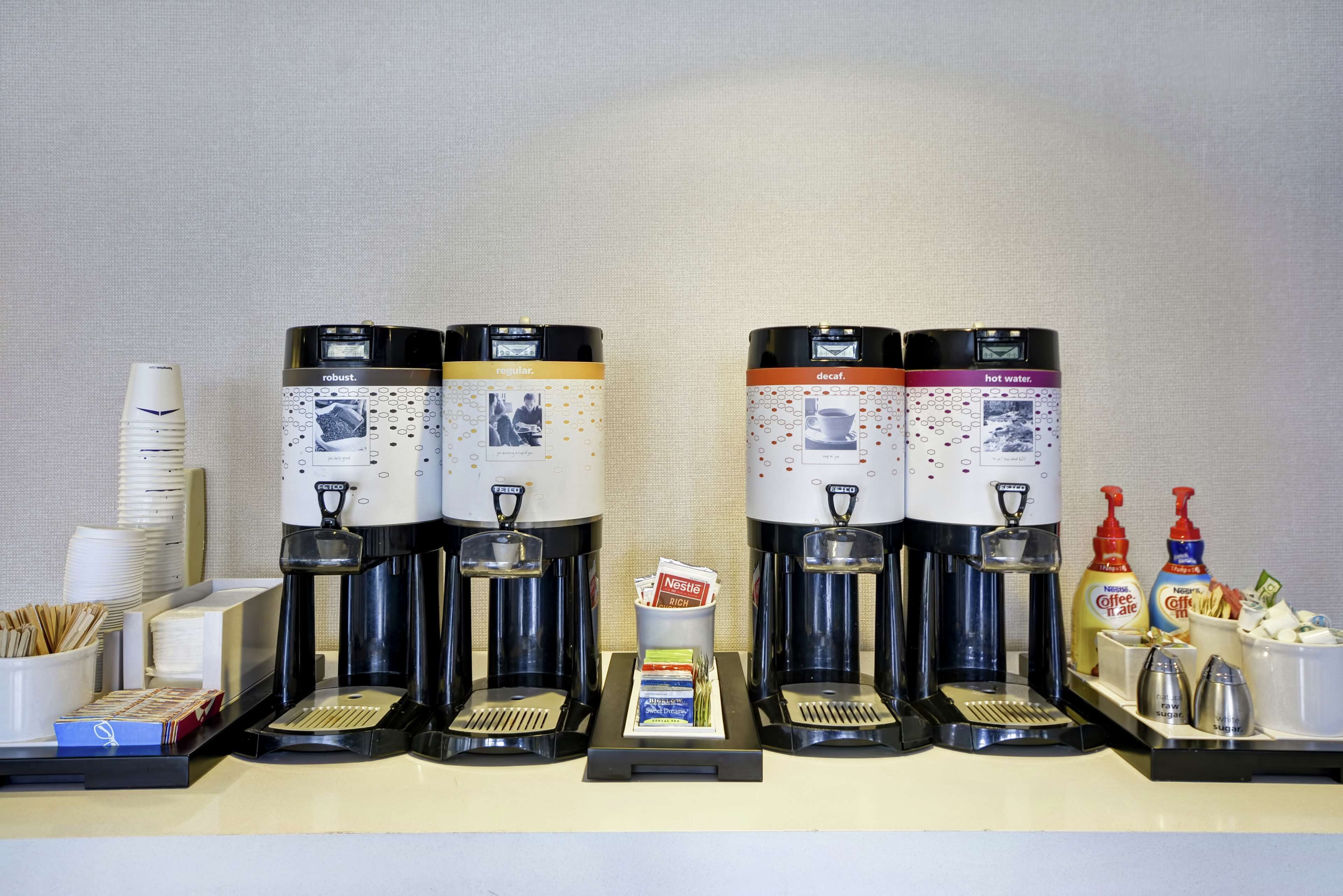 A coffee station with multiple coffee makers, disposable cups, and coffee pods.