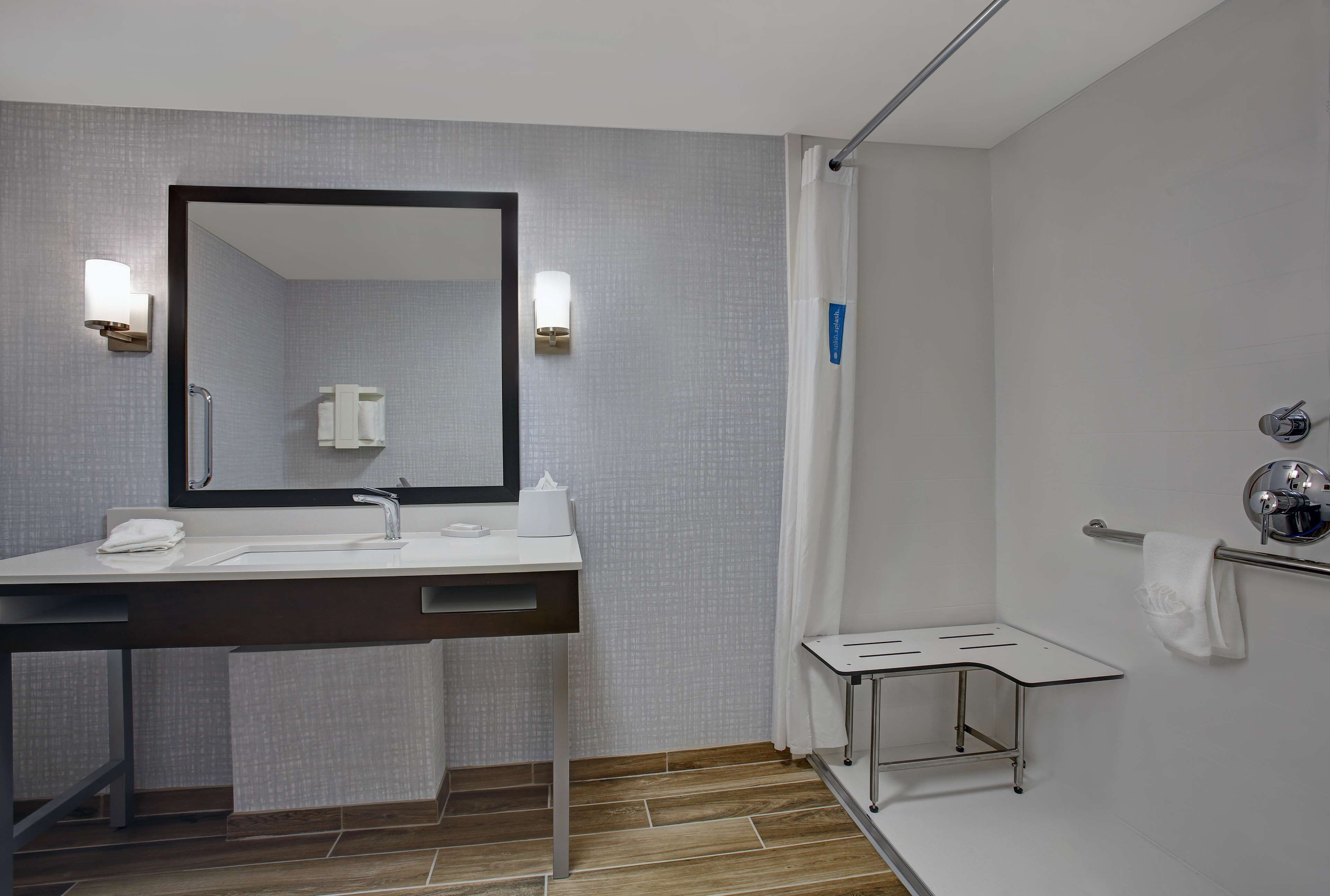 Un baño moderno con lavamanos, espejo, toallero y cortina de ducha.