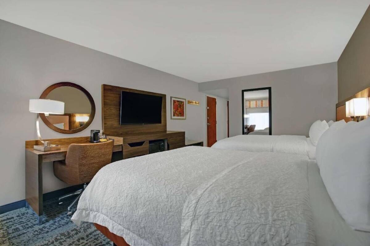 A hotel room with a bed, a desk with a chair, a television, and a mirror.