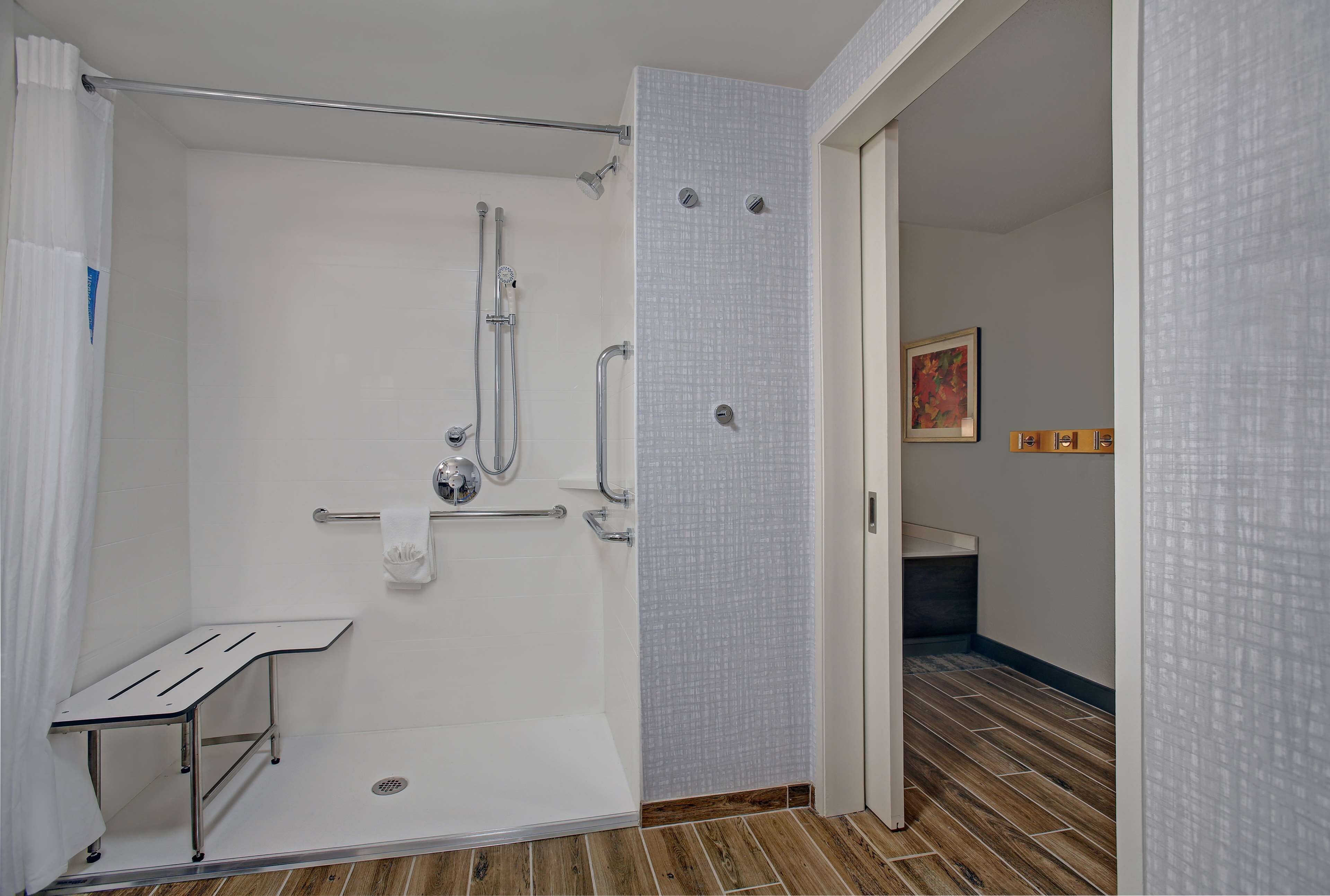 A walk-in shower with a grab bar, a towel rack, and a shower seat.