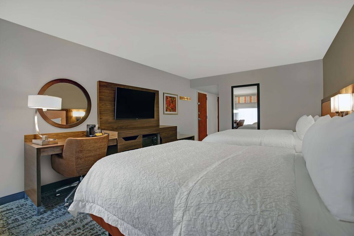 A hotel room with a large bed, a desk with a chair, a television, and a mirror.