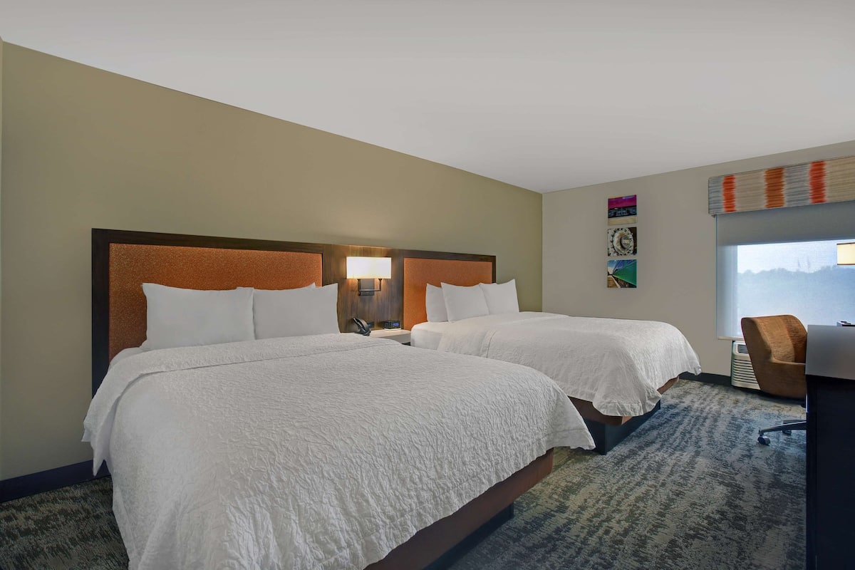 A hotel room with two beds, a desk, and a chair.