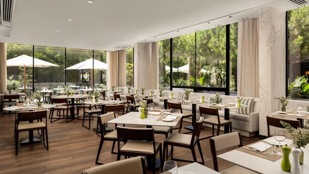 Un espace repas moderne, doté de tables et de chaises, de grandes fenêtres et de plantes d’intérieur.