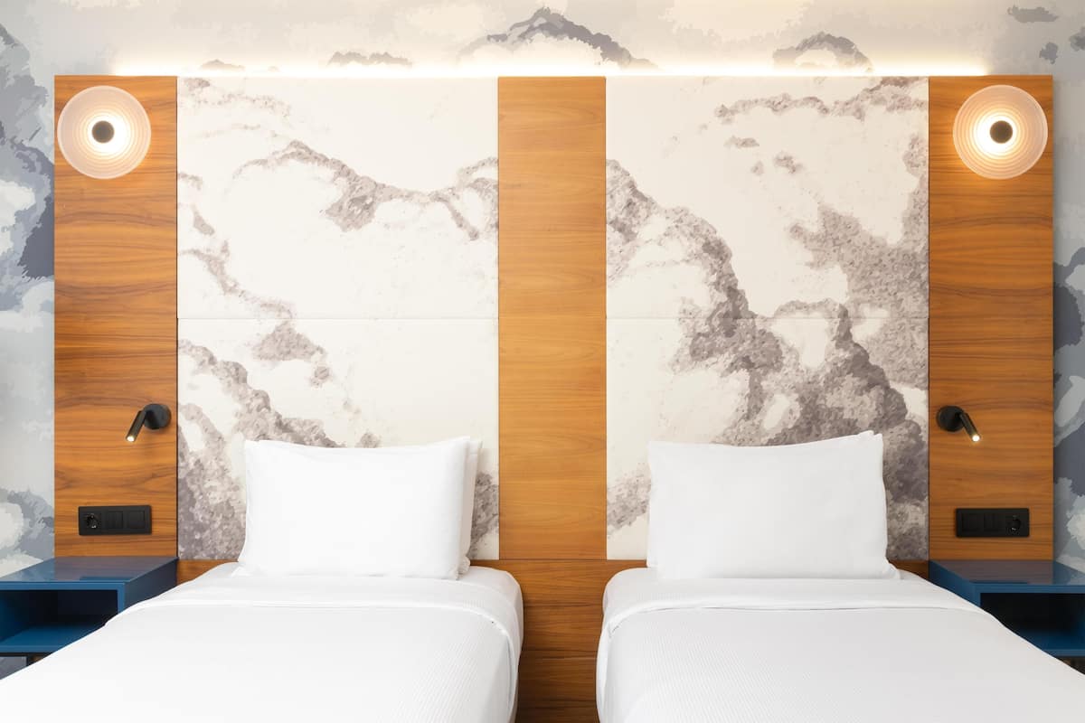A double room with two beds, wooden headboards, marble-patterned walls, and wall-mounted lights.