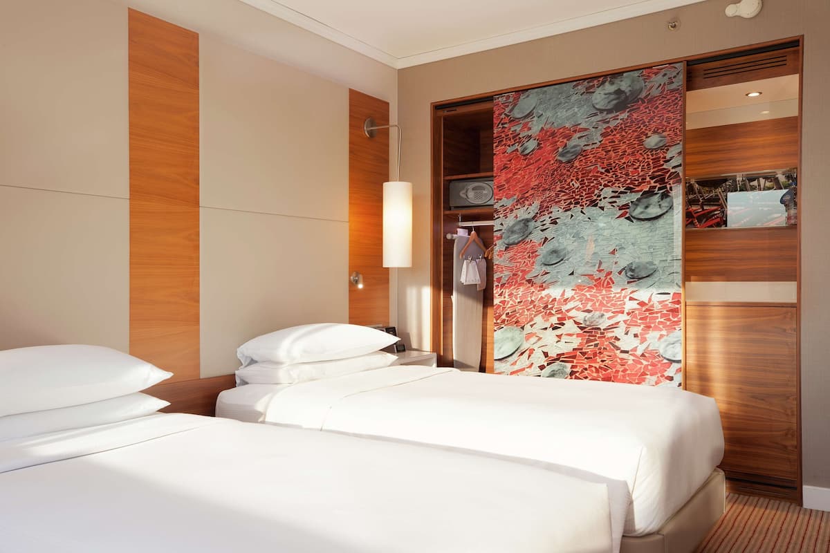 A hotel room with two beds, a wooden wardrobe, a decorative wall, and a hanging garment rack.