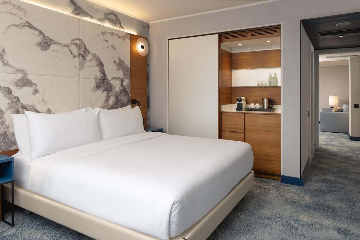 A hotel room with a large bed, a wooden wardrobe, a built-in desk, and a bathroom visible through an open door.