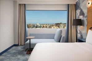A hotel room with a bed, a small table, a sofa, a lamp, and a view of the city. - Hilton Barcelona (Barcelona)