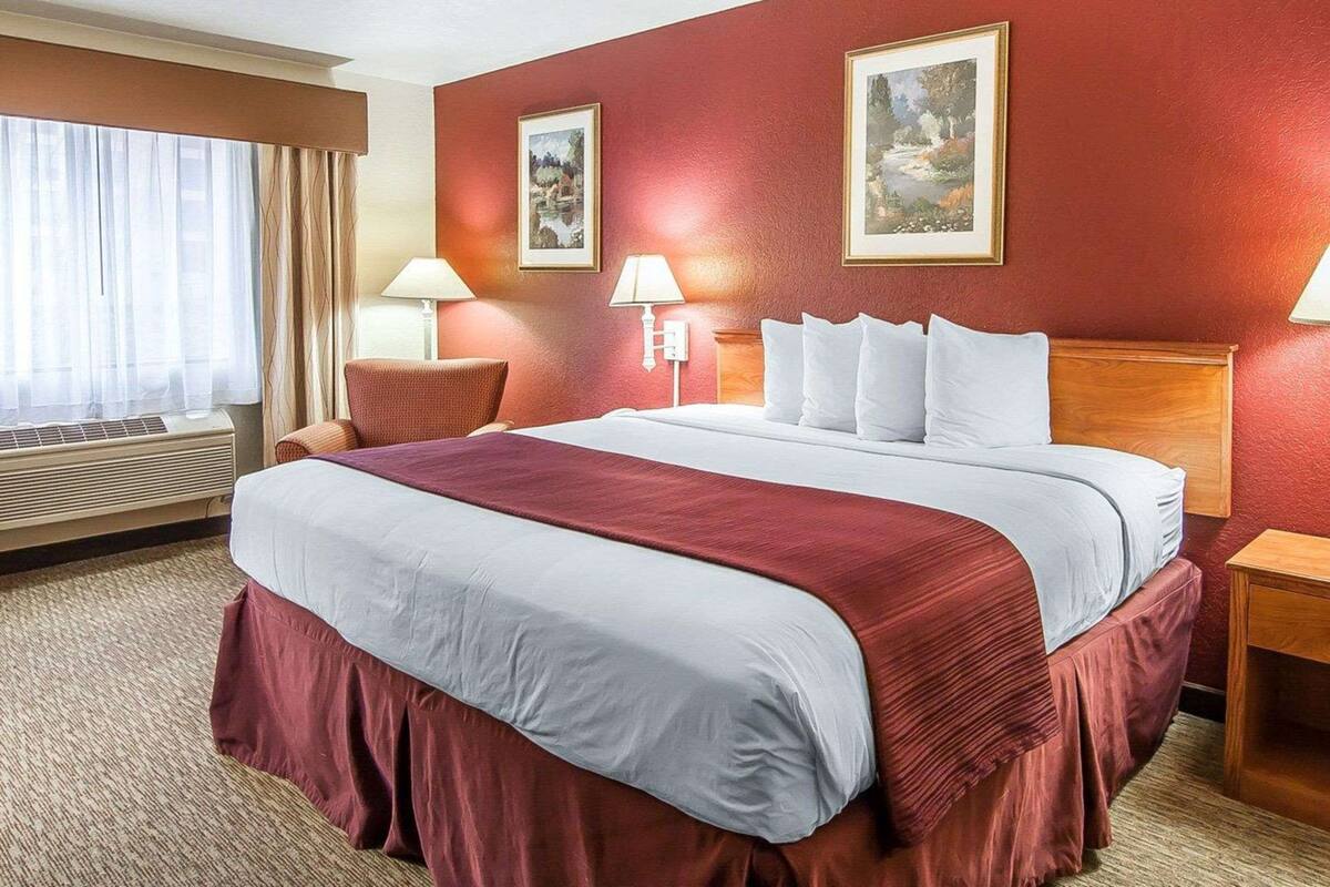 Habitación de hotel con una cama grande, dos lámparas de pared, una ventana con cortinas y dos cuadros en la pared.