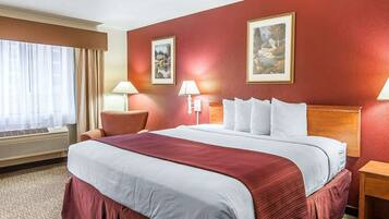 A hotel room with a large bed, two wall-mounted lamps, a window with curtains, and two framed pictures on the wall.