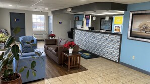 A reception area with a blue couch, a wooden table with a vase of flowers, and a reception desk with a digital screen. - Days Inn by Wyndham Perryville (Perryville)