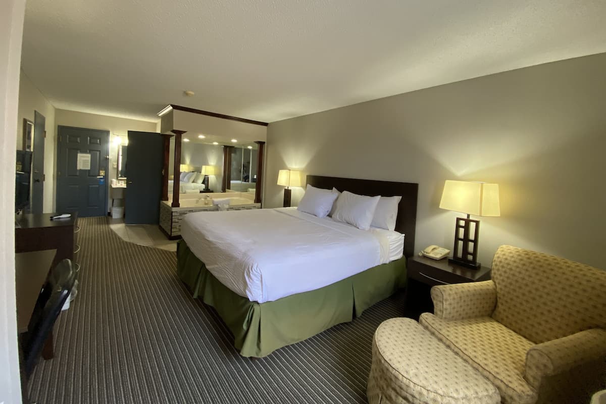 Een hotelkamer met een groot bed, een bureau, een stoel, een spiegel en een nachtkastje met een lamp.