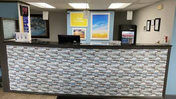 A reception desk with a mosaic tile design, a digital clock, a 'Hello Sunshine' sign, a refrigerator, and framed certificates on the wall.