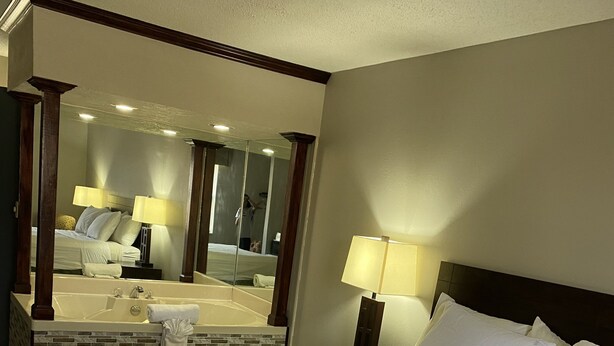 A hotel room with a large bed, a bathroom with a bathtub, and a mirror reflecting the room. - Days Inn by Wyndham Perryville (Perryville)