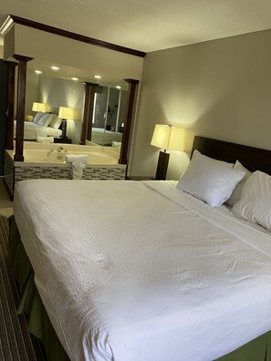 Habitación de hotel con una cama grande, baño con bañera y un espejo que refleja la habitación.