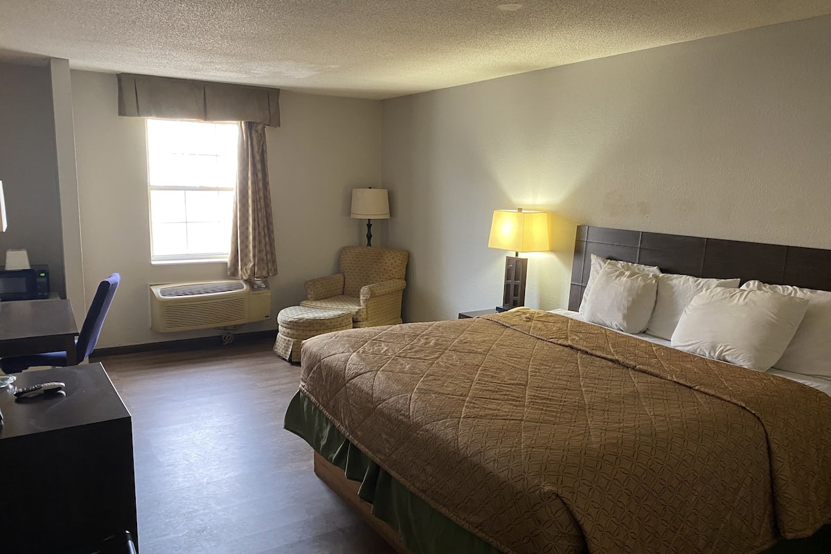 Een hotelkamer met een groot bed, een stoel, een bureau, een lamp en een raam met gordijnen.