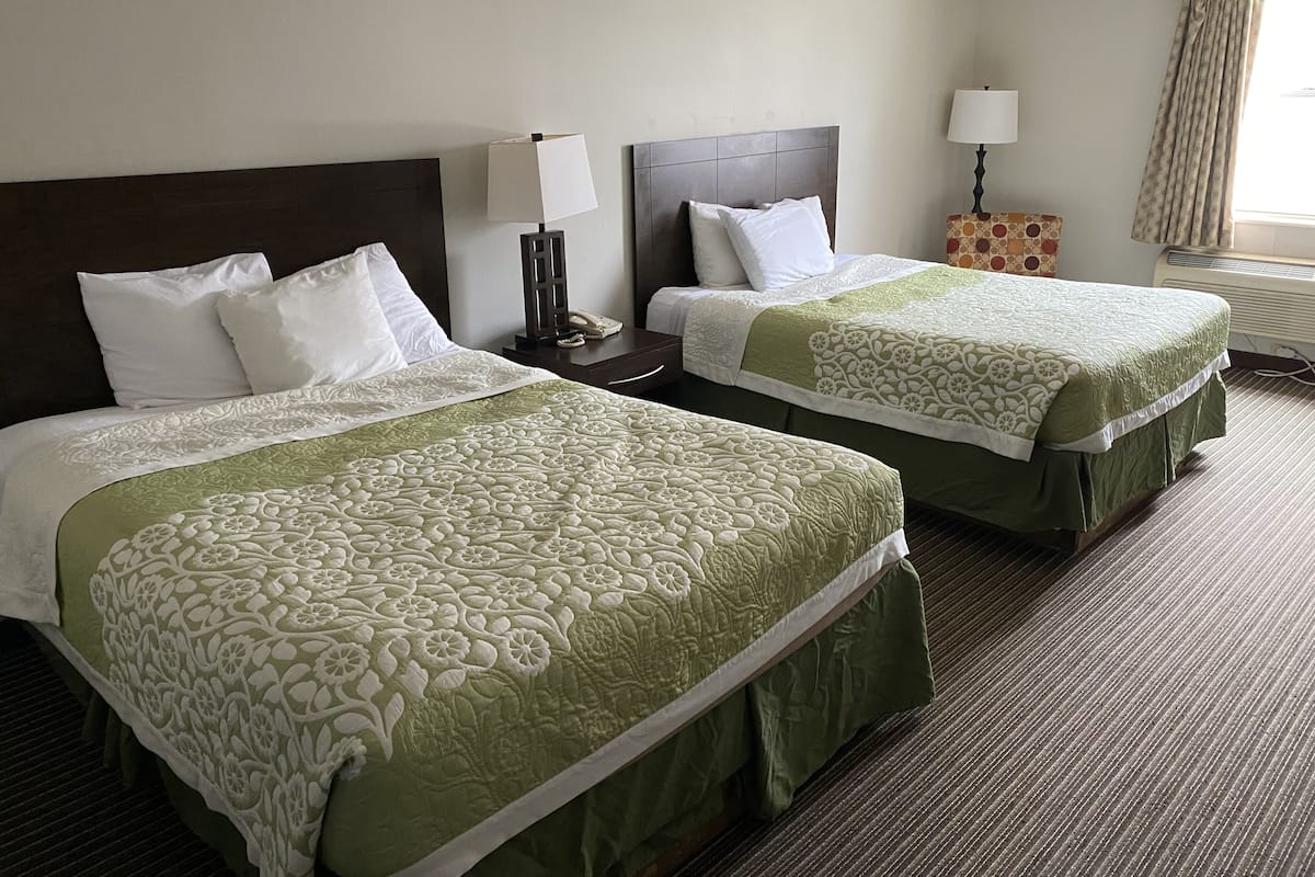 Hotelkamer met twee bedden, elk met een bloemenbedekking in groen en wit, een houten hoofdeinde, een nachtkastje met een lamp en een raam met gordijnen.