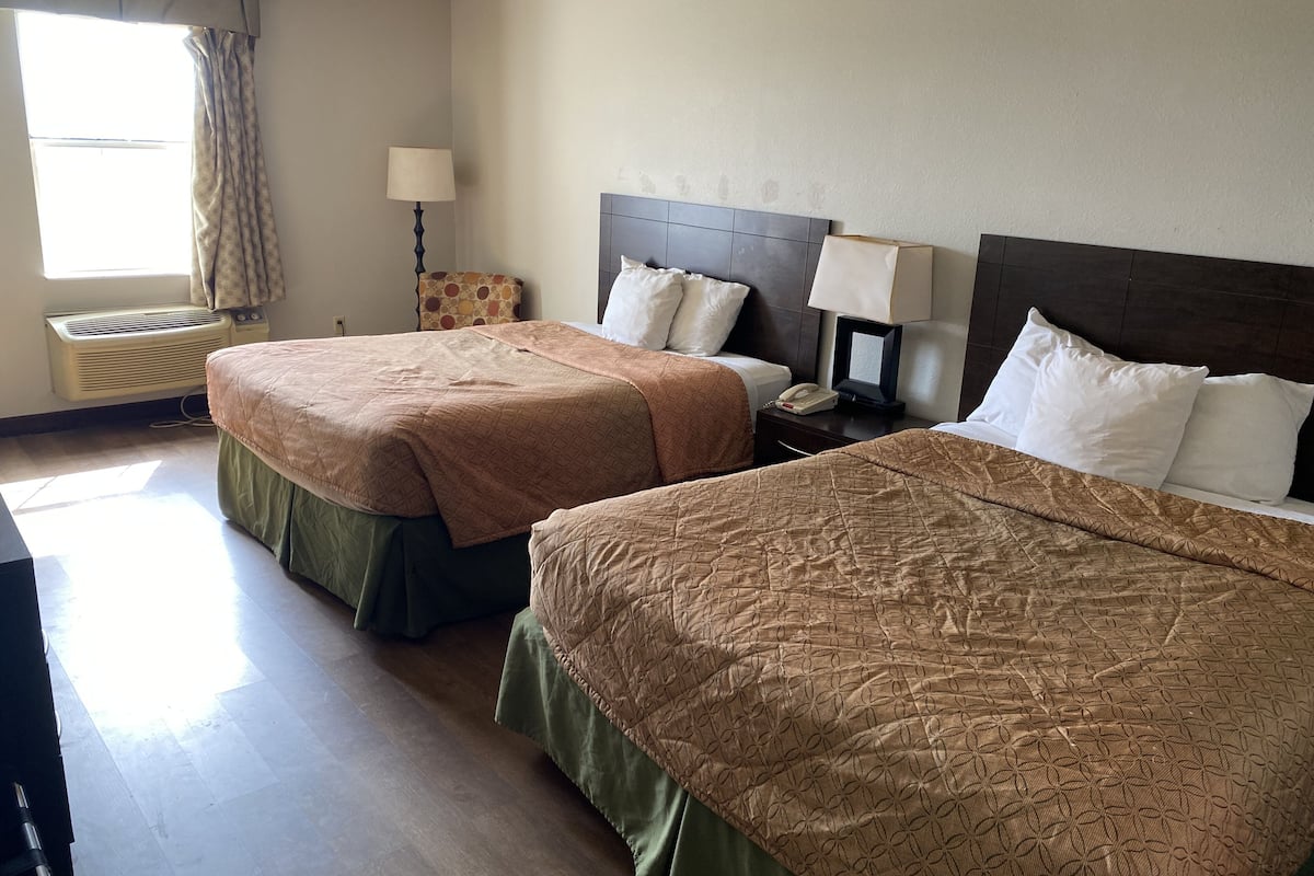 Een hotelkamer met twee bedden, een bedlampje, een telefoon en een raam met gordijnen.