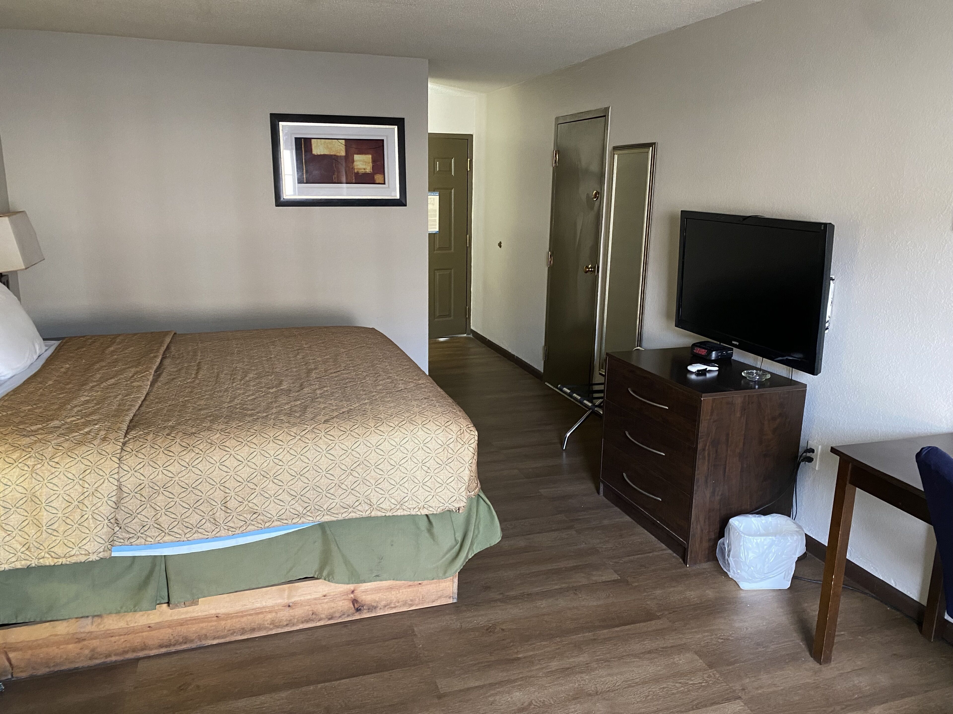 A hotel room with a bed, a dresser, a television, and a door leading to another room.