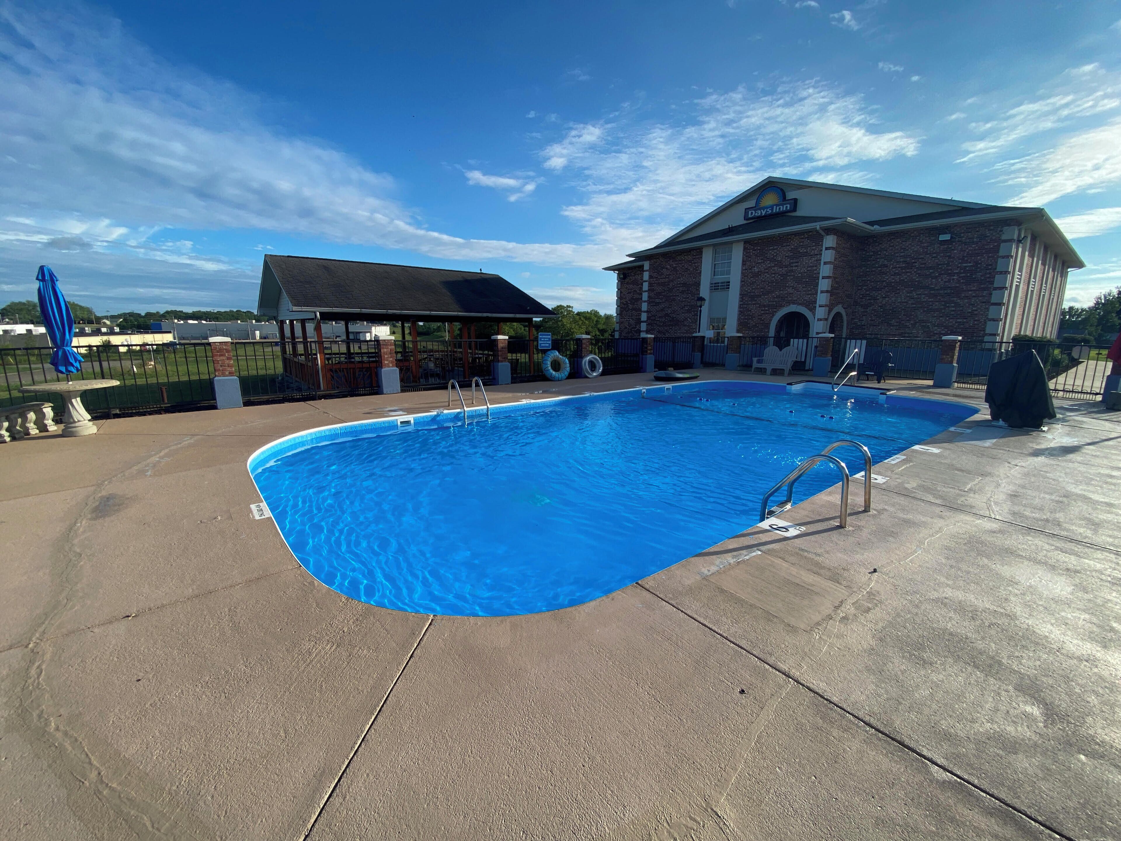 Una piscina con una cubierta azul, un edificio de ladrillo con el letrero de Days Inn, y un área de patio techada.
