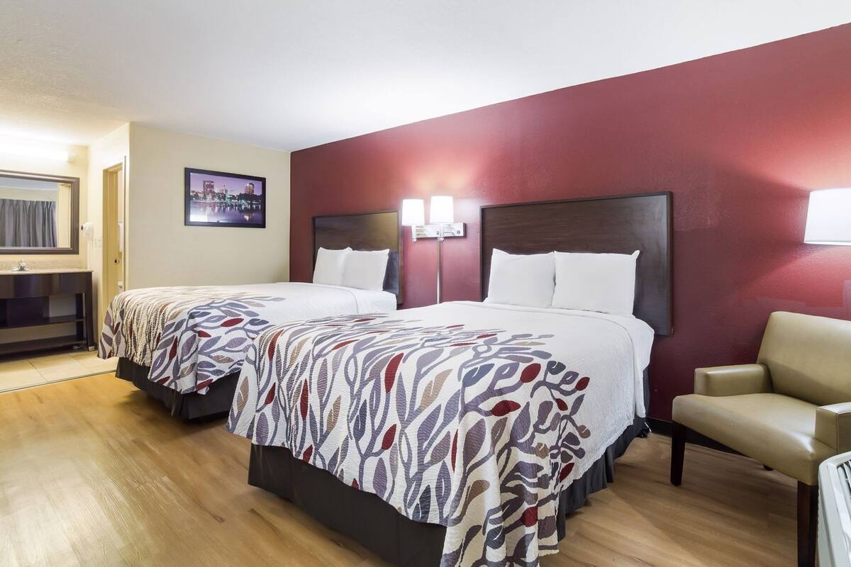 A hotel room with two beds, a desk, a chair, and a cityscape view.