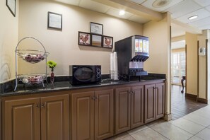 Una kitchenette con microondas, cafetera y una cesta de frutas.