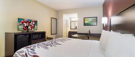 Una habitación de hotel con una cama, televisor, escritorio, microondas y espejo.