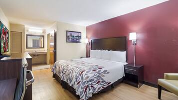 A hotel room with a bed, bedside tables, a desk, a chair, a mirror, and a picture on the wall.