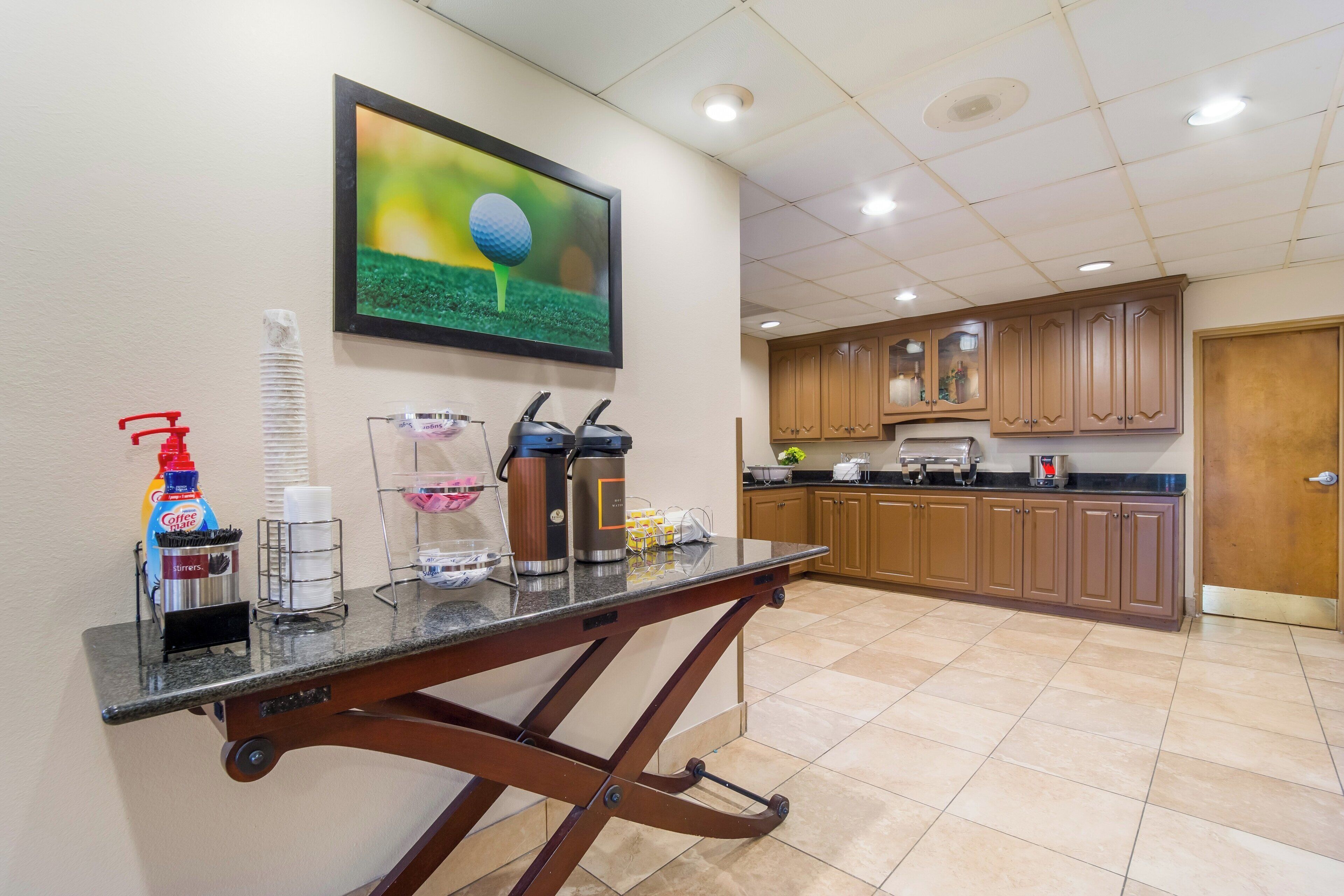 A kitchen area with a coffee station, a framed picture on the wall, and wooden cabinets.