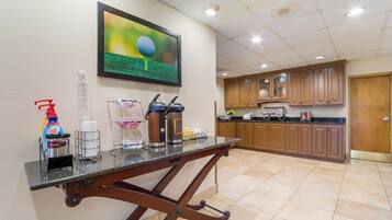 A kitchen area with a coffee station, a framed picture on the wall, and wooden cabinets.