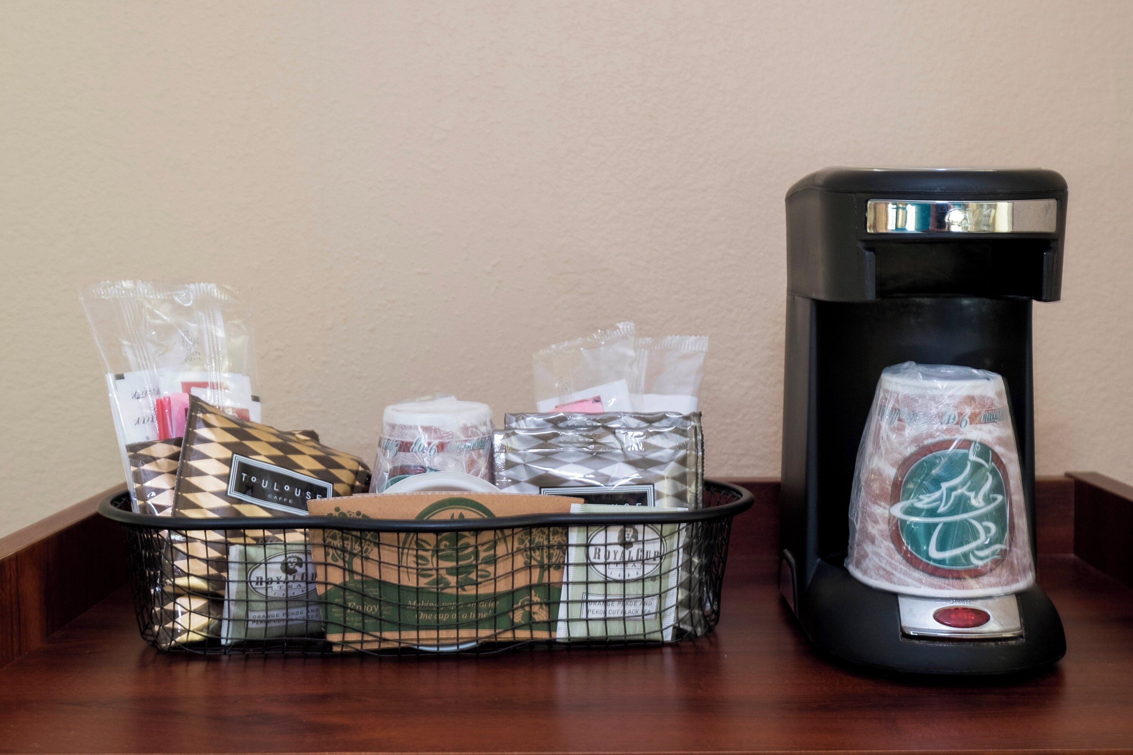 A coffee maker and a basket with various tea bags and a tea bag holder on a wooden surface.