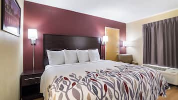 A hotel room with a large bed, a nightstand, a desk, a chair, a window with curtains, and wall-mounted lamps.