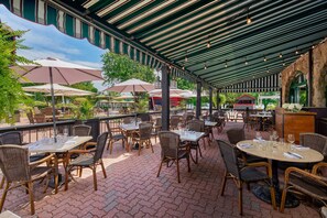 Une terrasse extérieure avec des tables et des chaises, des parasols et un sol en briques.