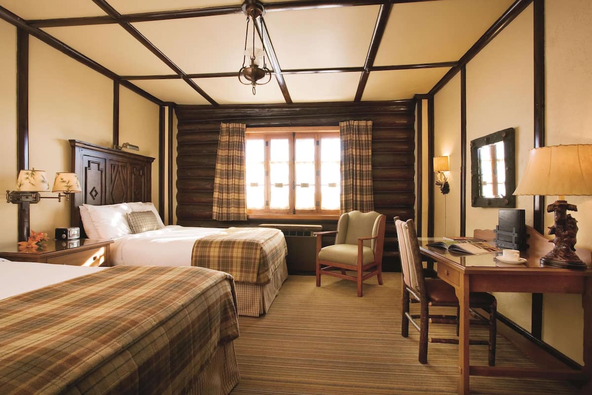 Een hotelkamer met twee bedden, een bureau, een stoel, een lamp en een raam met gordijnen.