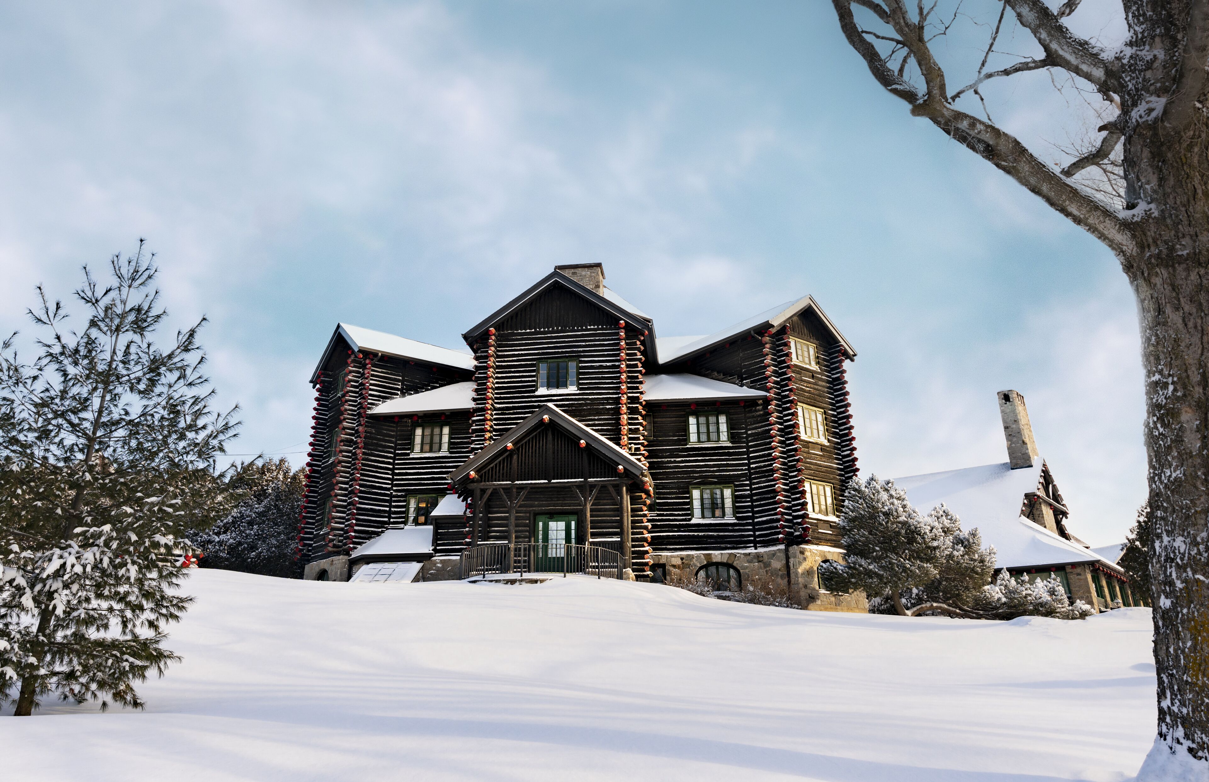 Un edificio grande de estilo cabaña de troncos con fachada simétrica, múltiples chimeneas y un paisaje cubierto de nieve.